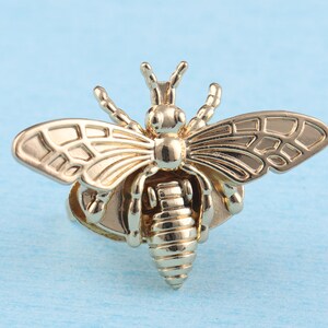 May include: A gold-toned bee ring with detailed wings and a textured body. The ring is a statement piece with a unique design.