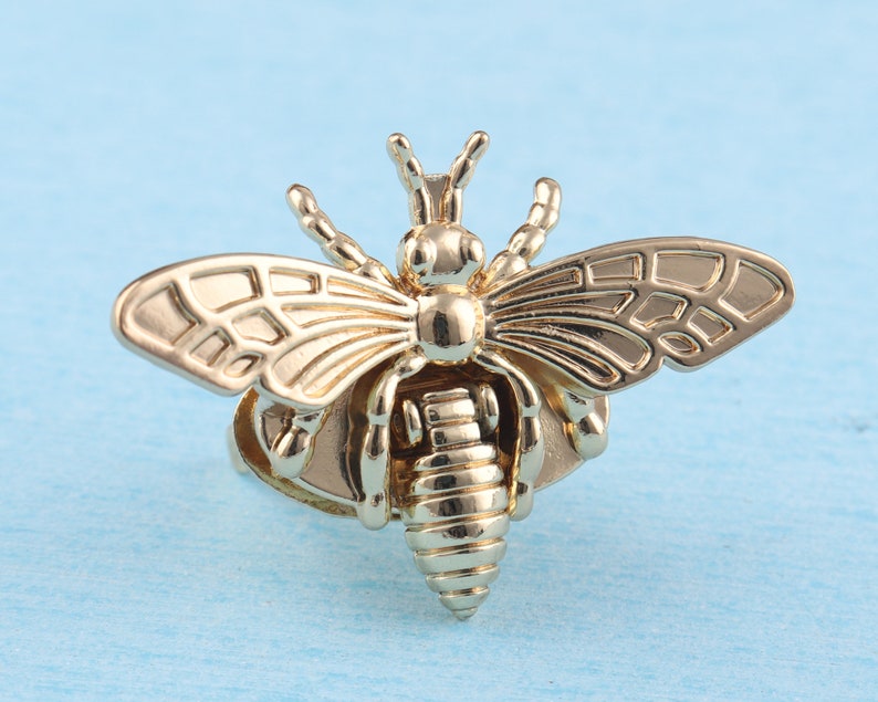 May include: A gold-toned bee ring with detailed wings and a textured body. The ring is a statement piece with a unique design.