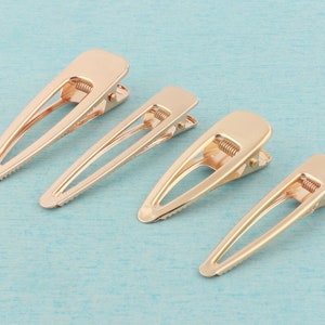 May include: Four gold metal hair clips of varying sizes. The clips are all the same design, with a smooth, oval-shaped head and a spring-loaded mechanism.