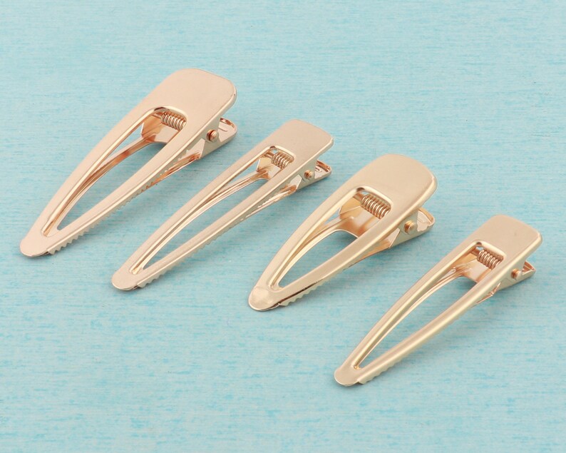 May include: Four gold metal hair clips of varying sizes. The clips are all the same design, with a smooth, oval-shaped head and a spring-loaded mechanism.