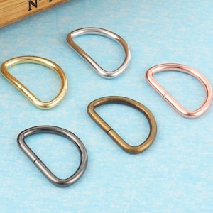 May include: Five different metal D-rings in various finishes: silver, gold, black, and rose gold. The rings are all the same size and shape.