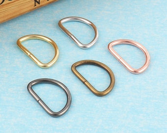 May include: Five different metal D-rings in various finishes: silver, gold, black, and rose gold. The rings are all the same size and shape.