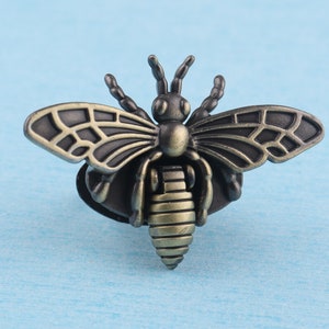 May include: A bronze-colored bee brooch with detailed wings and a textured body. The bee is a popular symbol of hard work and community.