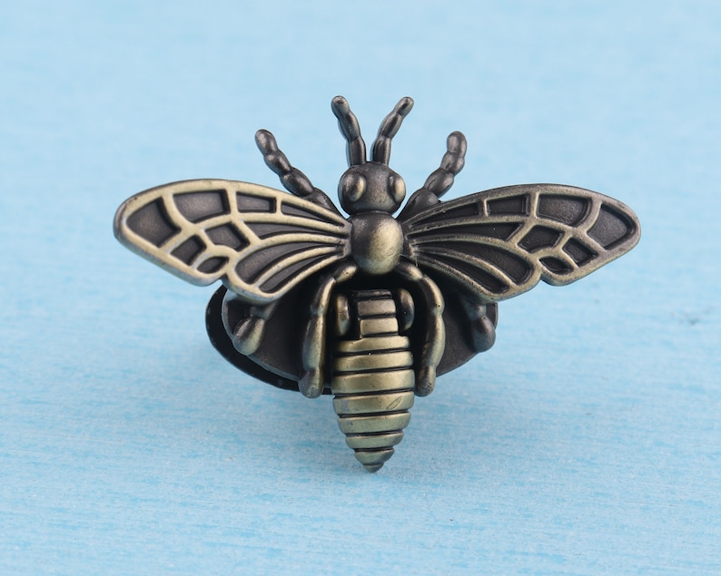 May include: A bronze-colored bee brooch with detailed wings and a textured body. The bee is a popular symbol of hard work and community.