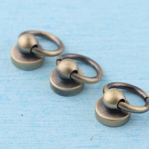 May include: Three antique gold-toned metal rings with a round ball at the top. The rings are attached to a flat, round base.