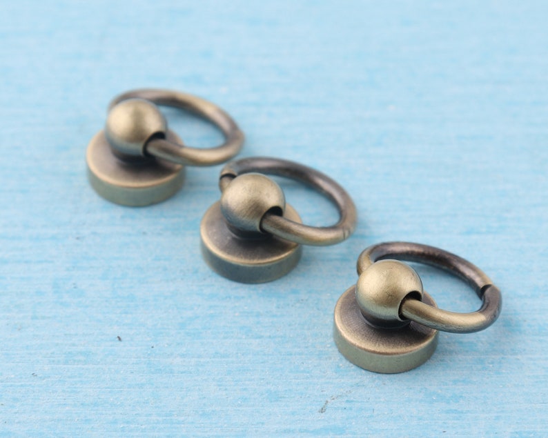 May include: Three antique gold-toned metal rings with a round ball at the top. The rings are attached to a flat, round base.