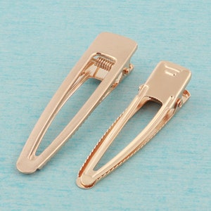 May include: Two gold metal hair clips. The clips are about 2 inches long and have a simple, oval shape.