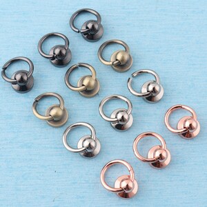 May include: Assortment of metal rings with a ball on top. The rings are in various finishes, including silver, gold, and black.