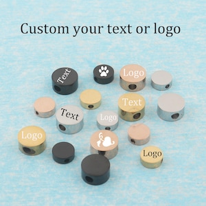 Puede incluir: Una colección de pequeñas cuentas metálicas cilíndricas en tonos negro, oro, oro rosa y plata. Algunas cuentas presentan texto, logotipos o iconos grabados como una huella o una hoja. El texto "Custom your text or logo" aparece impreso.