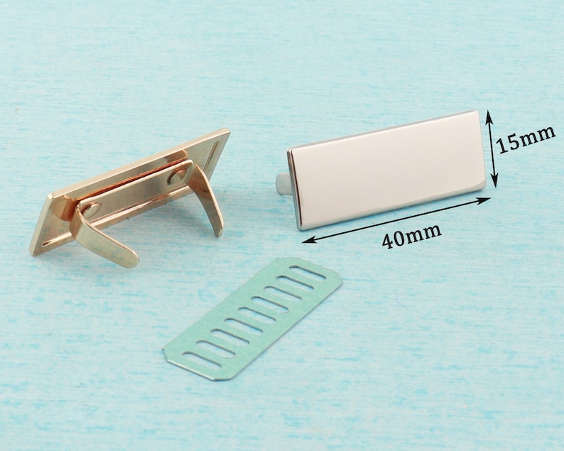May include: Two gold-toned metal clasps with a rectangular shape and a spring mechanism. A separate piece of metal with a grid pattern is also shown. The clasps measure 40 mm by 15 mm.