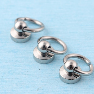 May include: Three silver metal swivel snap hooks with a round base. The hooks are on a light blue surface.