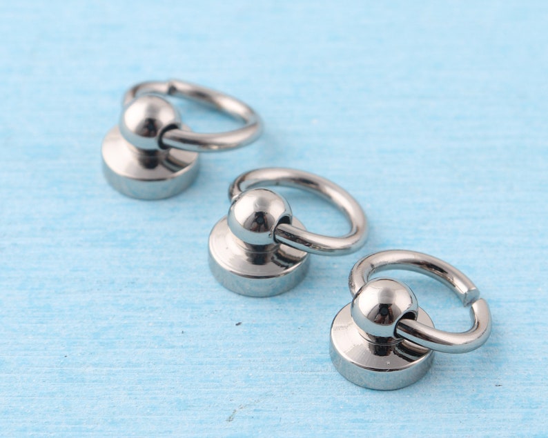 May include: Three silver metal swivel snap hooks with a round base. The hooks are on a light blue surface.