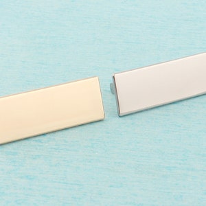 May include: Two rectangular metal name tags, one gold and one silver, on a light blue background.