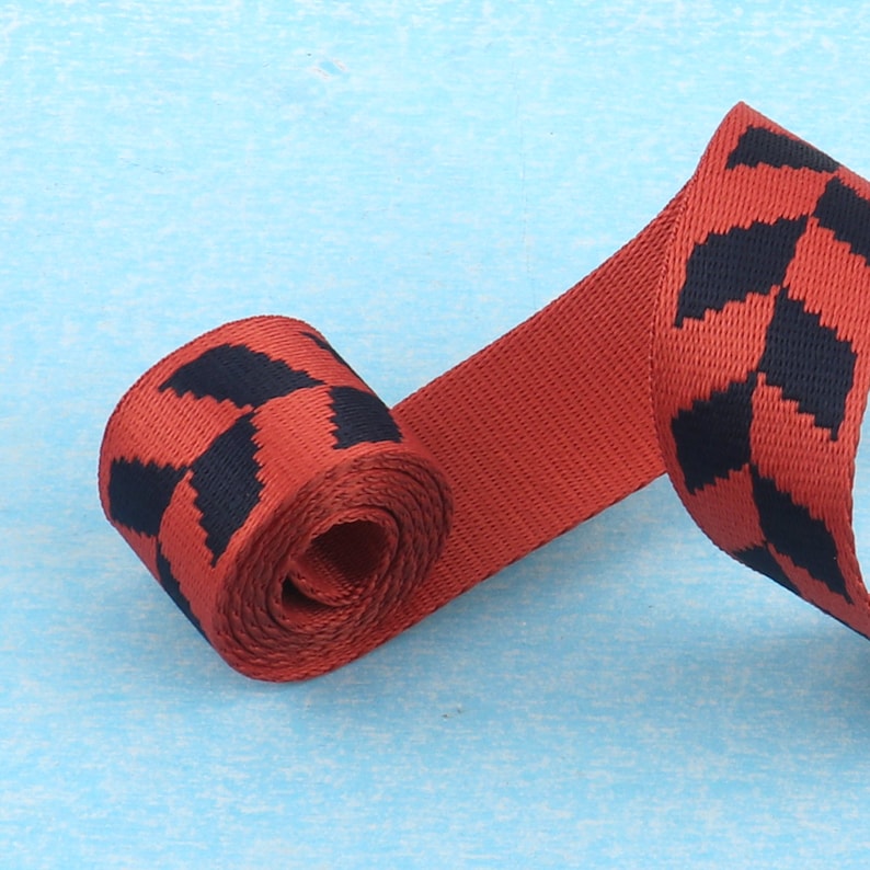 May include: Red and black patterned webbing with a geometric design. The webbing is rolled up and the pattern is visible on both sides.