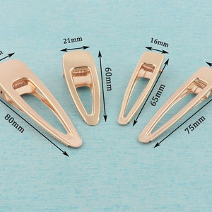 May include: Four gold metal hair clips of different sizes. The clips are 21 mm, 16 mm, 16 mm, and 23 mm wide. The clips are 60 mm, 65 mm, 75 mm, and 80 mm long.