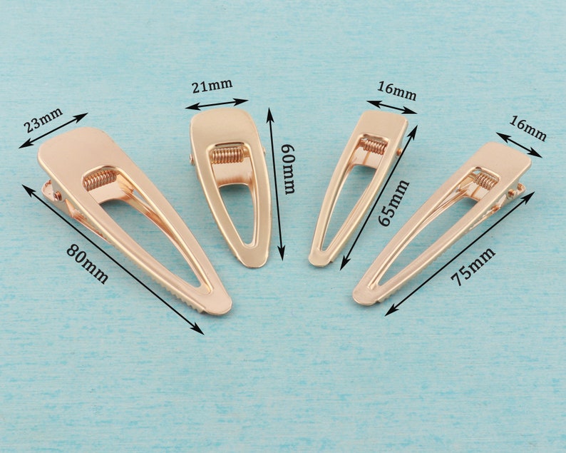 May include: Four gold metal hair clips of different sizes. The clips are 21 mm, 16 mm, 16 mm, and 23 mm wide. The clips are 60 mm, 65 mm, 75 mm, and 80 mm long.