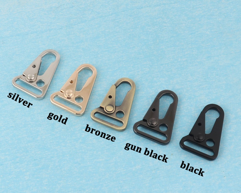 Puede incluir: Una colecci&oacute;n de cierres giratorios met&aacute;licos en varios colores: plata, oro, bronce, negro ca&ntilde;&oacute;n y negro. Cada cierre tiene un gancho triangular y un lazo rectangular. Los colores est&aacute;n etiquetados debajo de cada cierre.