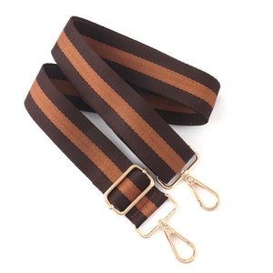 Pode incluir: Uma al&ccedil;a ajust&aacute;vel com listras marrons e bege e fechos de metal dourado. A al&ccedil;a &eacute; feita de tecido tecido e tem um visual casual.