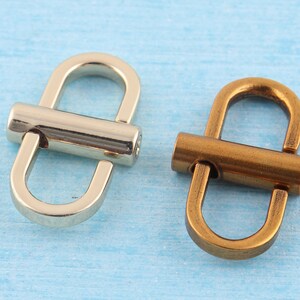 May include: Two metal D-ring clasps, one silver and one bronze. The clasps are made of a smooth metal and have a rounded shape.