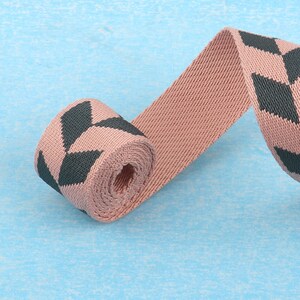 May include: Pink and dark green woven ribbon with a geometric pattern. The ribbon is rolled up and the ends are loose.