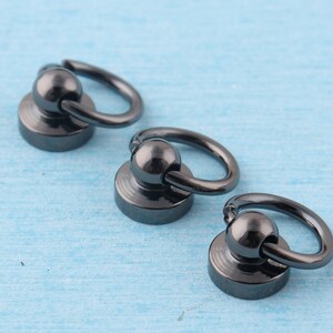 May include: Three black metal swivel snap hooks with a round base. The hooks are attached to a black metal ring.