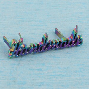 Op de afbeelding: Regenboogkleurige metalen tag met het woord "Handmade" in een cursief schrift.
