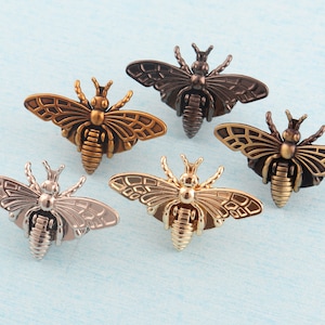 May include: Five decorative metal bee charms in different finishes, including gold, silver, and bronze. The bees have detailed wings and bodies.