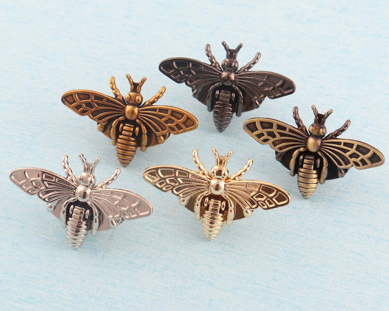 May include: Five decorative metal bee charms in different finishes, including gold, silver, and bronze. The bees have detailed wings and bodies.