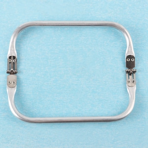 Puede incluir: Un marco de bolso de mano de metal plateado con dos bisagras sobre un fondo azul claro.