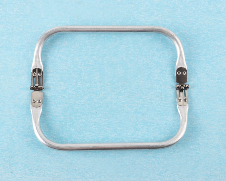 Puede incluir: Un marco de bolso de mano de metal plateado con dos bisagras sobre un fondo azul claro.