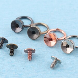 May include: Assortment of metal hardware findings, including rings, screw-on caps, and screw-on rings. The findings are in various finishes, including silver, gold, and black.