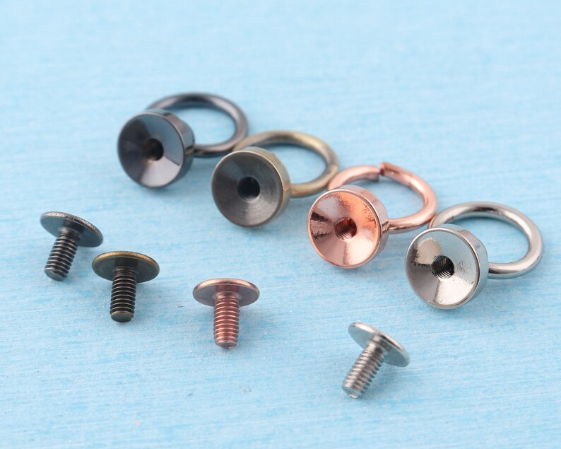 May include: Assortment of metal hardware findings, including rings, screw-on caps, and screw-on rings. The findings are in various finishes, including silver, gold, and black.