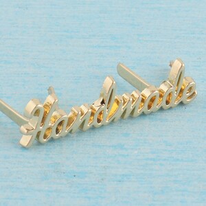 Op de afbeelding: Goudkleurig metalen "Handmade" label met twee pinnen aan de achterkant om aan een product te bevestigen.