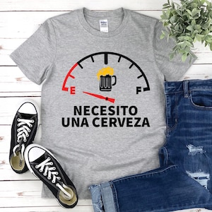 May include: Gray t-shirt with a fuel gauge graphic and the text "Necesito una cerveza" in black. The gauge is filled with a beer mug icon.