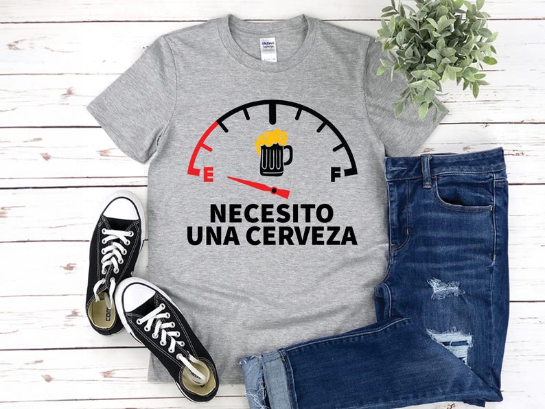 May include: Gray t-shirt with a fuel gauge graphic and the text "Necesito una cerveza" in black. The gauge is filled with a beer mug icon.