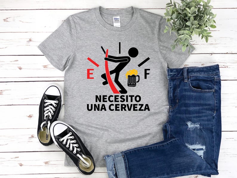 May include: A gray t-shirt with a graphic of a fuel gauge with a stick figure pushing a beer mug. The text on the shirt reads "Necesito una cerveza".