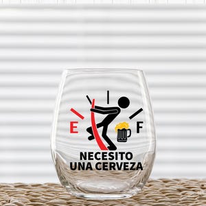 May include: A clear glass with a red and black fuel gauge graphic that reads "Necesito una cerveza" which translates to "I need a beer".
