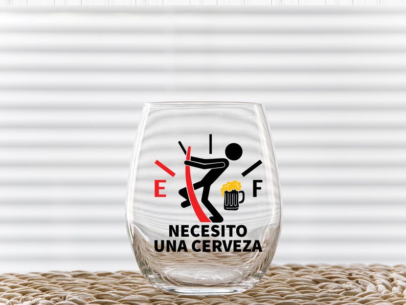 May include: A clear glass with a red and black fuel gauge graphic that reads "Necesito una cerveza" which translates to "I need a beer".