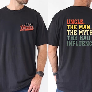 May include: Black t-shirt with "COOL Uncles CLUB" in red script on the front and "UNCLE. THE MAN. THE MYTH. THE BAD INFLUENCE." in colorful text on the back. A casual tee for a fun uncle.