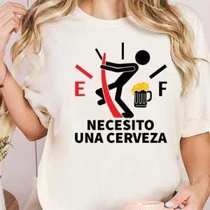 May include: White t-shirt with a black and red gas gauge graphic. The gauge is empty and a stick figure is pushing a beer mug into the gauge. The text "Necesito una cerveza" is printed below the graphic.