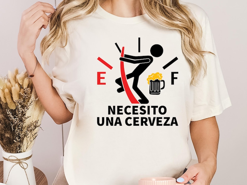 May include: White t-shirt with a black and red gas gauge graphic. The gauge is empty and a stick figure is pushing a beer mug into the gauge. The text "Necesito una cerveza" is printed below the graphic.