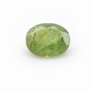 Könnte beinhalten: Ein oval geschliffener Edelstein in hellem Grün. Der Stein liegt vor einem weißen Hintergrund, der seine Klarheit und Farbe hervorhebt. Der Schliff des Edelsteins zeigt mehrere Facetten.