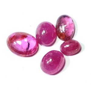 Puede incluir: Cinco gemas rosas pulidas, de forma ovalada, con un acabado brillante. Las gemas varían ligeramente en tamaño y tono, algunas mostrando patrones internos. Las piedras están sobre un fondo blanco.
