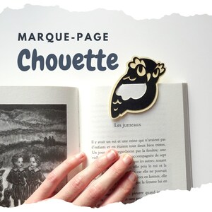 Könnte beinhalten: Ein schwarzer und beigefarbener Eulen-Lesezeichen befindet sich auf den Seiten eines offenen Buches. Das Lesezeichen ist aus Holz und hat ein ausgeschnittenes Design. Das Buch hat schwarz-weiße Illustrationen und französischen Text. Der Text "MARQUE-PAGE Chouette" steht oben.