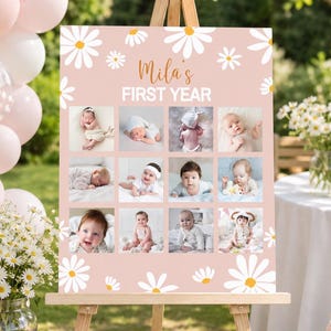 May include: A rectangular pink sign featuring white daisy illustrations and the text "Mila's FIRST YEAR" in white and orange. The sign displays a grid of twelve individual photographs of a baby at different stages of their first year.