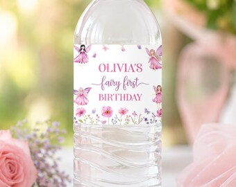 May include: A clear plastic water bottle with a white cap and a custom label featuring pink fairy illustrations, floral accents, and the text Olivia's fairy first birthday printed in pink and dark pink lettering on a white background.