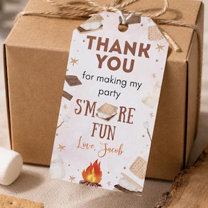 May include: A brown cardboard gift box tied with twine and a rectangular paper tag featuring the text THANK YOU for making my party S'MORE FUN Love, Jacob, decorated with illustrations of s'mores, a campfire, and small gold stars.