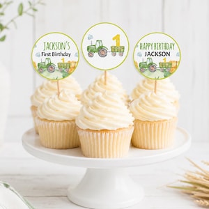 Könnte beinhalten: Drei Cupcakes mit runden Papieraufsteckern, die grüne Aquarell-Traktoren, gelbe Einsen sowie den Text Jackson's First Birthday und Happy Birthday Jackson zeigen, präsentiert auf einem weißen Tortenständer.