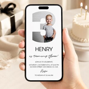 Op de afbeelding: Een digitale verjaardagsuitnodiging op een smartphonescherm met een groot cijfer drie en een foto van een jong kind met een gamecontroller. De tekst luidt Henry is turning three, join us to celebrate, Saturday, October 15th, at 2:00 PM, 123 Main Street, San Diego, CA, 1345, RSVP to Megan at 123.456.789.