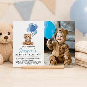 Op de afbeelding: Een rechthoekige verjaardagsuitnodigingskaart met een aquarelillustratie van een bruine teddybeer die blauwe ballonnen met het cijfer &eacute;&eacute;n vasthoudt. De tekst luidt Huson's BEAR-Y 1ST BIRTHDAY, Sunday, November 12th, at 2:00 PM, Huson's House, 123 Main Street, Los Angeles, CA 1235, RSVP to Ashley at 123.456.789. Rechts staat een foto van een kind in een berenkostuum met een blauwe ballon.